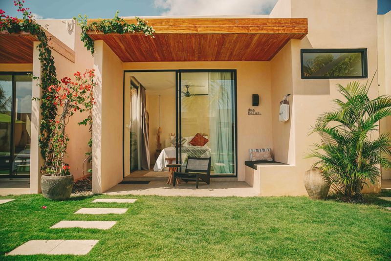 A sunlit studio terrace with a timber awning, bougainvillea and a garden path